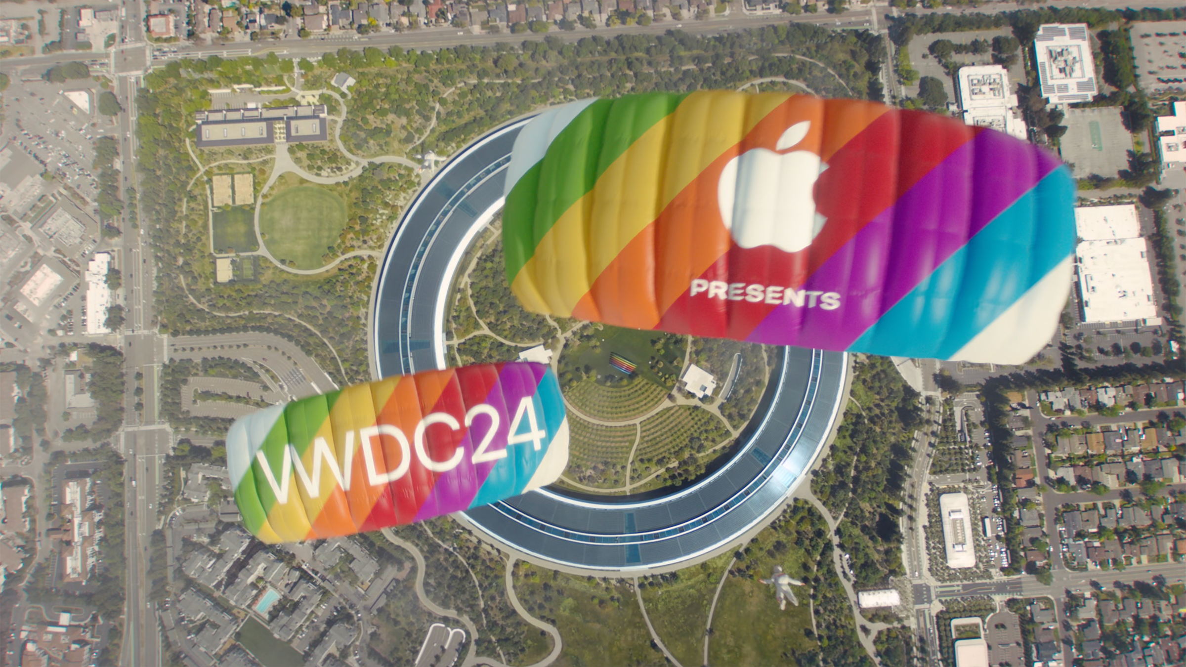 Skydivers with rainbow striped parachutes that read 'Apple presents WWDC24'